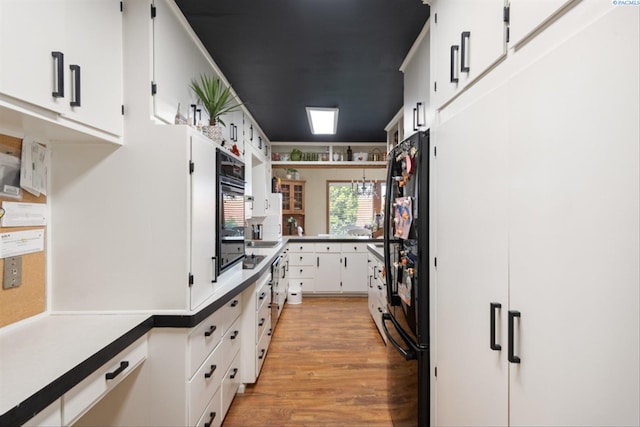 kitchen with white cabinetry, black refrigerator, and light hardwood / wood-style floors