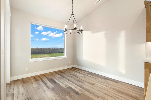 unfurnished dining area with a notable chandelier, vaulted ceiling, and light wood-type flooring