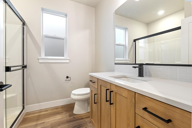 bathroom featuring hardwood / wood-style flooring, tasteful backsplash, vanity, toilet, and walk in shower