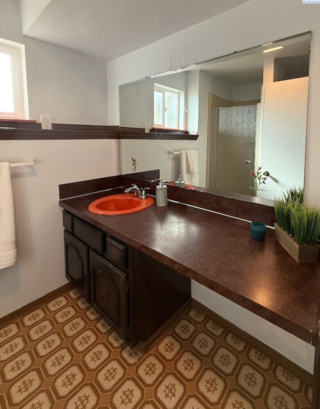 bathroom with a shower with shower door, vanity, and baseboards