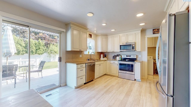 kitchen featuring backsplash, light wood-type flooring, a sink, light stone counters, and stainless steel appliances