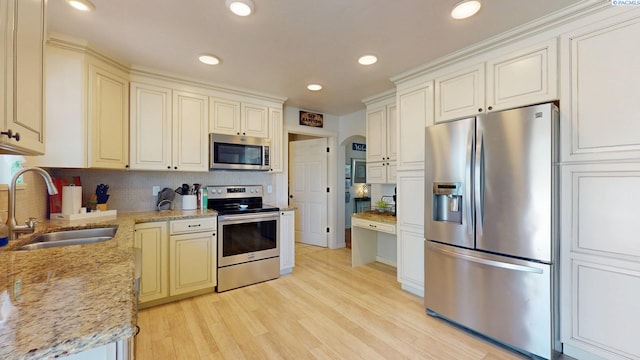 kitchen with backsplash, light stone countertops, light wood-type flooring, a sink, and stainless steel appliances