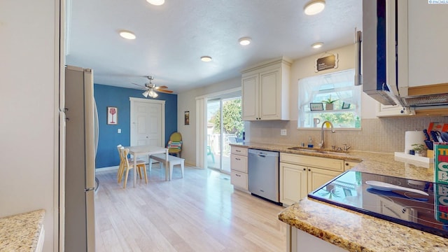 kitchen featuring appliances with stainless steel finishes, a sink, light wood-style floors, a ceiling fan, and backsplash
