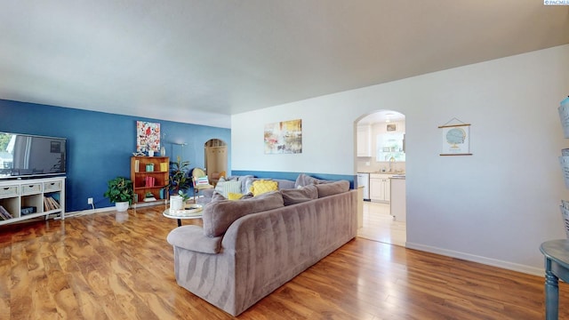 living area featuring baseboards, arched walkways, light wood-style flooring, and a wealth of natural light