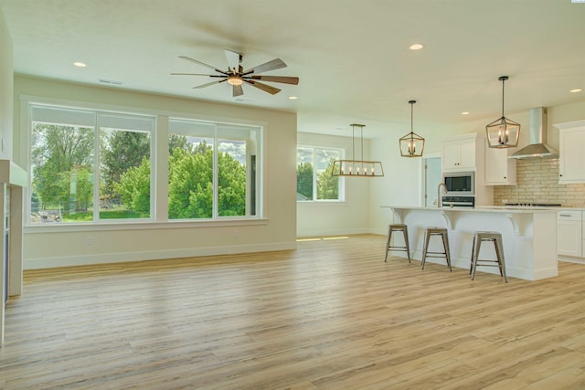 9418 Balflour Ct, Pasco, WA 99301 - kitchen with wall chimney range hood, stainless steel microwave, a breakfast bar, decorative backsplash, and light countertops