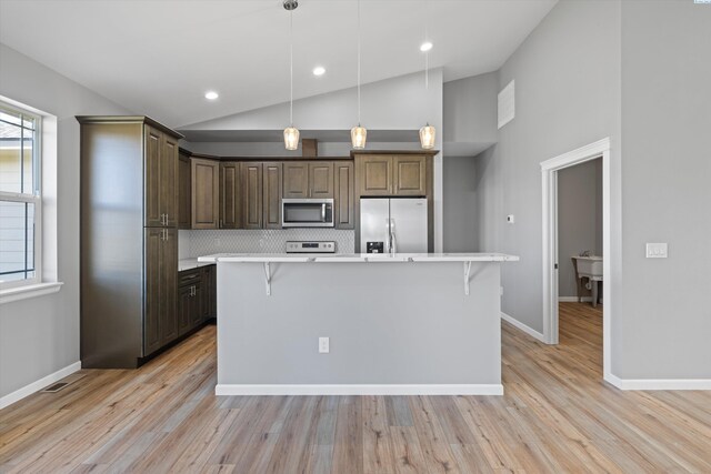 kitchen featuring pendant lighting, dark brown cabinets, stainless steel appliances, a kitchen breakfast bar, and a kitchen island