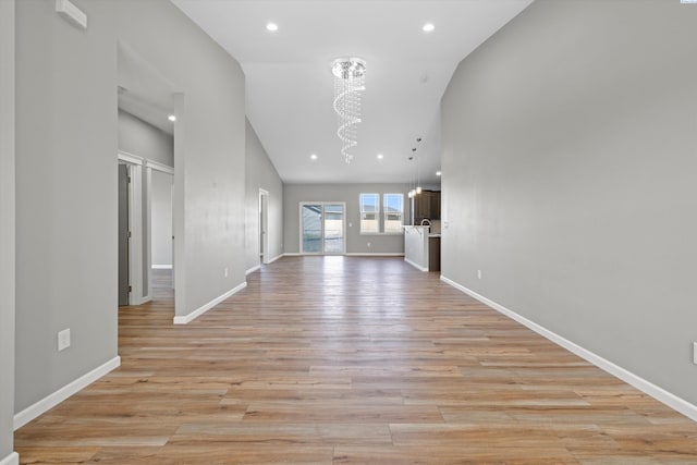 unfurnished living room with a chandelier, high vaulted ceiling, and light hardwood / wood-style flooring