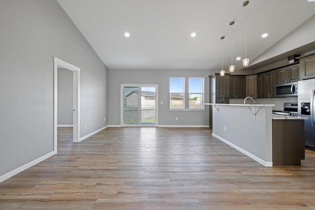 kitchen featuring appliances with stainless steel finishes, decorative light fixtures, an island with sink, a kitchen bar, and dark brown cabinetry