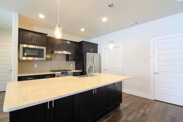 kitchen with stainless steel appliances, under cabinet range hood, tasteful backsplash, dark wood-style floors, and a large island with sink