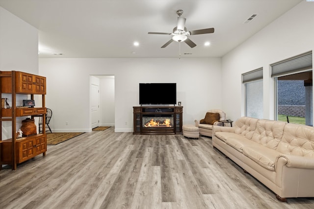 living area with recessed lighting, visible vents, a glass covered fireplace, light wood-type flooring, and baseboards