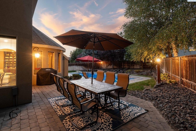 patio terrace at dusk featuring area for grilling and a fenced in pool