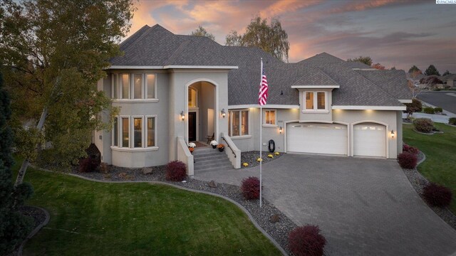 view of front of home with driveway, stucco siding, roof with shingles, an attached garage, and a front yard