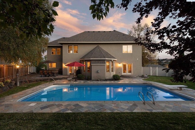 pool at dusk with french doors, a lawn, a patio area, and a fenced backyard