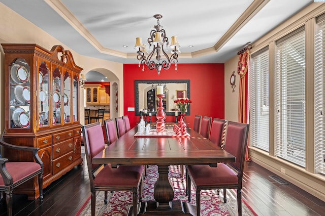 dining area with dark wood-type flooring, a raised ceiling, and a notable chandelier