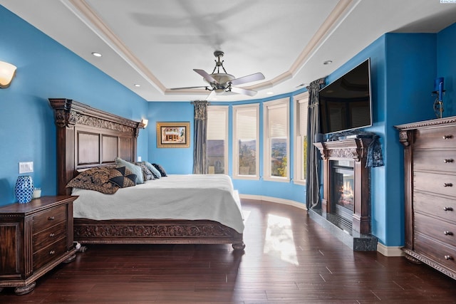 bedroom with dark hardwood / wood-style floors, ceiling fan, and a tray ceiling