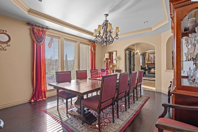 dining area featuring a notable chandelier, dark hardwood / wood-style floors, ornamental molding, and a raised ceiling