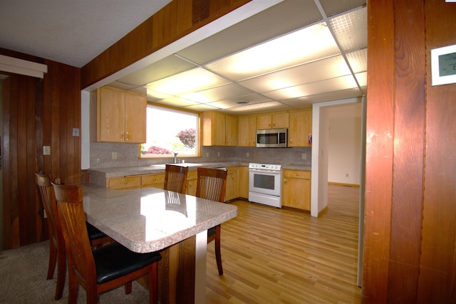 kitchen with white range with electric stovetop, light wood-style floors, light countertops, stainless steel microwave, and decorative backsplash