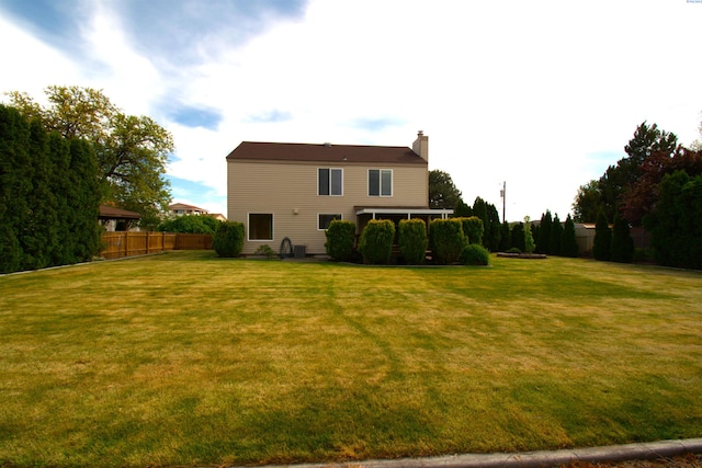 back of house with fence, a yard, and a chimney