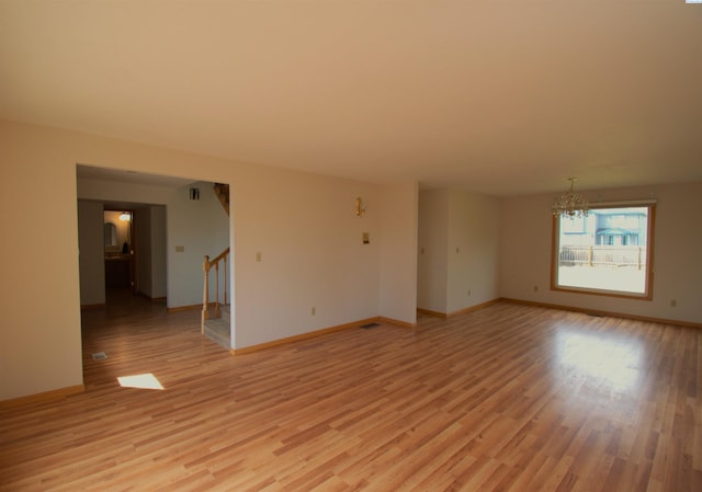 unfurnished room with baseboards, a notable chandelier, stairway, and light wood-type flooring