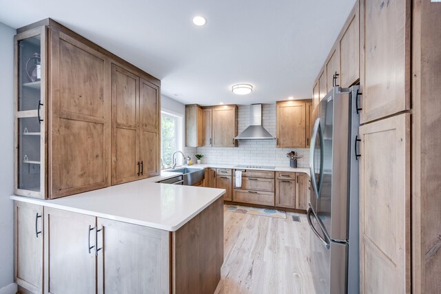 495 NW Robert St, Pullman, WA 99163 - kitchen with freestanding refrigerator, wall chimney range hood, a peninsula, light wood-style flooring, and tasteful backsplash