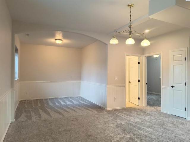 carpeted spare room with arched walkways, wainscoting, and visible vents