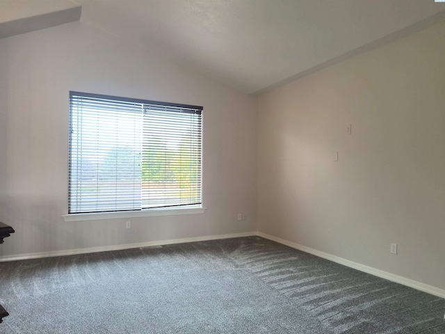 spare room featuring lofted ceiling, dark carpet, and baseboards