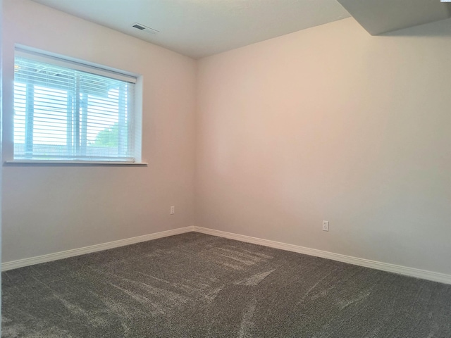 empty room featuring dark colored carpet, visible vents, and baseboards