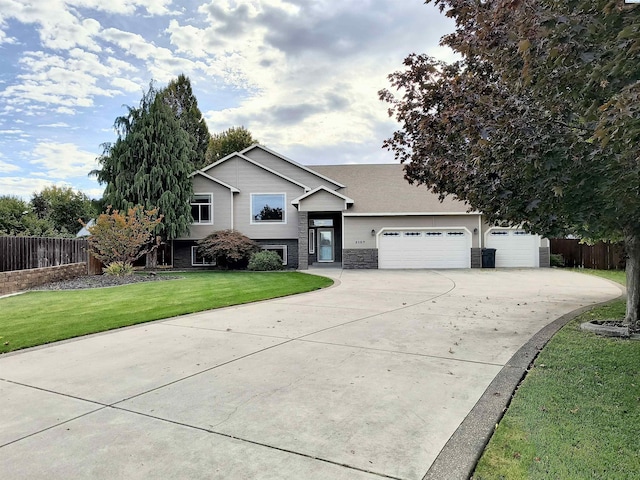 split level home with a garage, concrete driveway, stone siding, fence, and a front lawn