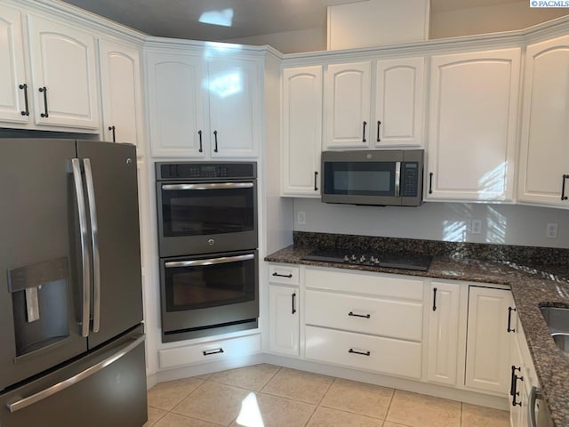 kitchen with light tile patterned floors, stainless steel appliances, dark stone counters, and white cabinets