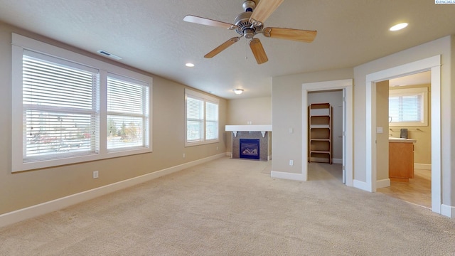 unfurnished living room featuring light carpet, ceiling fan, and a textured ceiling