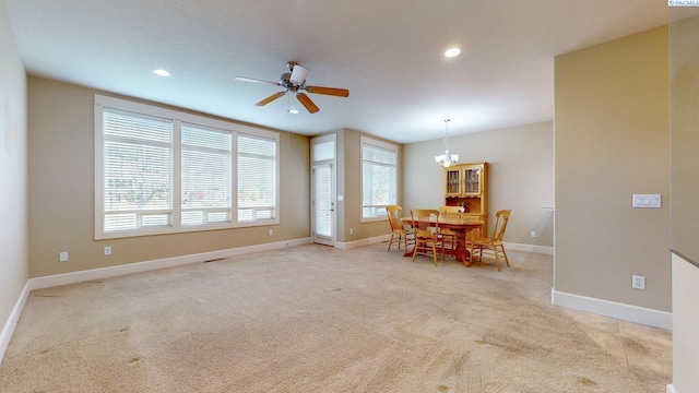 dining area featuring light colored carpet, ceiling fan with notable chandelier, and a wealth of natural light