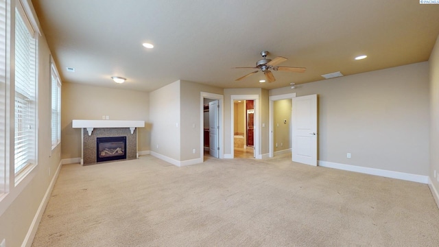 unfurnished living room with ceiling fan, light colored carpet, and a tiled fireplace