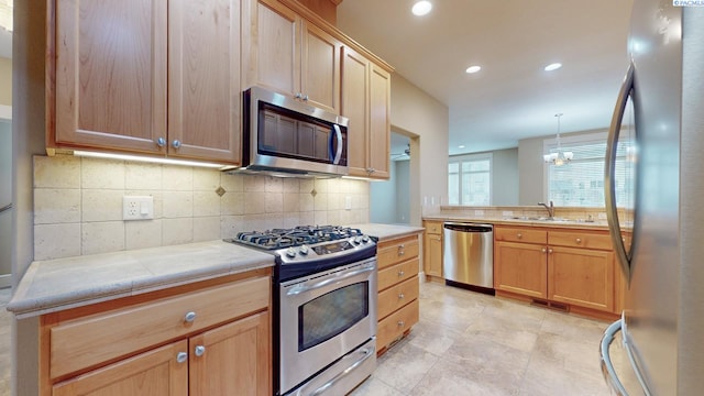 kitchen featuring pendant lighting, sink, backsplash, stainless steel appliances, and light brown cabinets