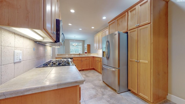 kitchen with appliances with stainless steel finishes, light brown cabinetry, decorative light fixtures, sink, and kitchen peninsula