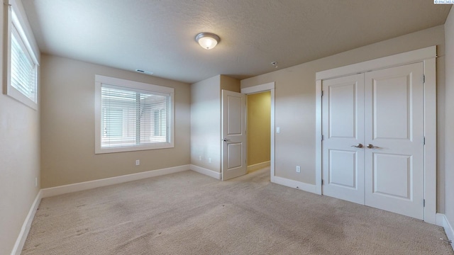 unfurnished bedroom with light carpet, a closet, and a textured ceiling