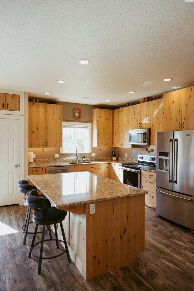 kitchen featuring sink, dark wood-type flooring, appliances with stainless steel finishes, a center island, and light stone counters