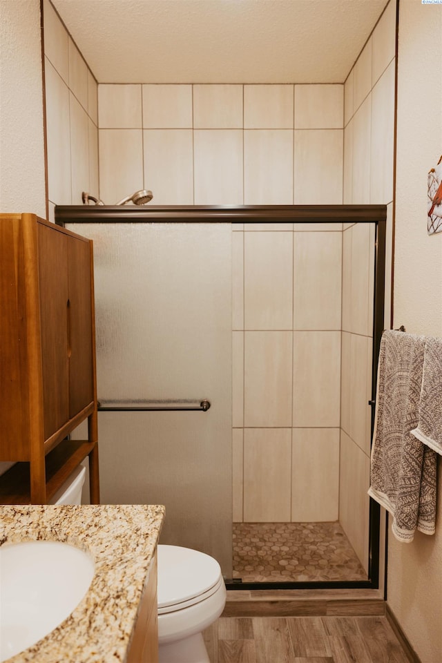 bathroom with wood-type flooring, tiled shower, vanity, and toilet