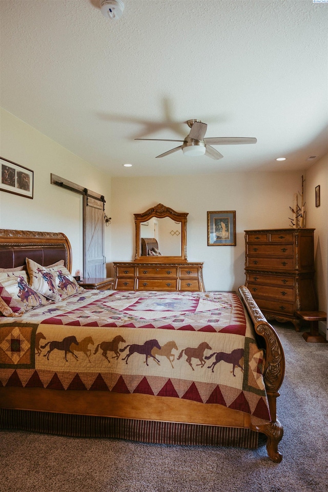 bedroom featuring ceiling fan, a barn door, carpet floors, and a textured ceiling