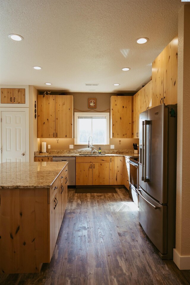 kitchen featuring dark hardwood / wood-style floors, sink, stainless steel appliances, light stone countertops, and a textured ceiling