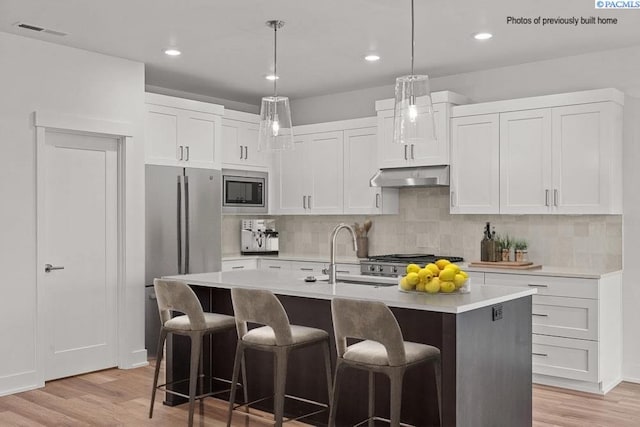2817 Avrio Ave, Richland, WA 99354 - kitchen with a sink, under cabinet range hood, stainless steel appliances, light wood finished floors, and a kitchen bar