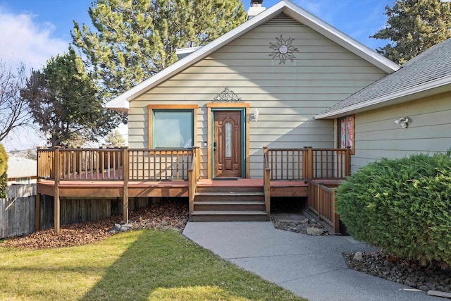 view of front of house featuring a shingled roof, a deck, and a front lawn