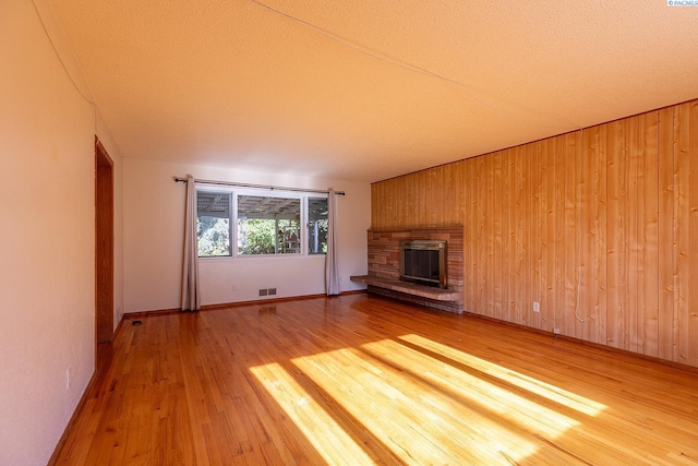 unfurnished living room featuring wood-type flooring, a stone fireplace, and wood walls