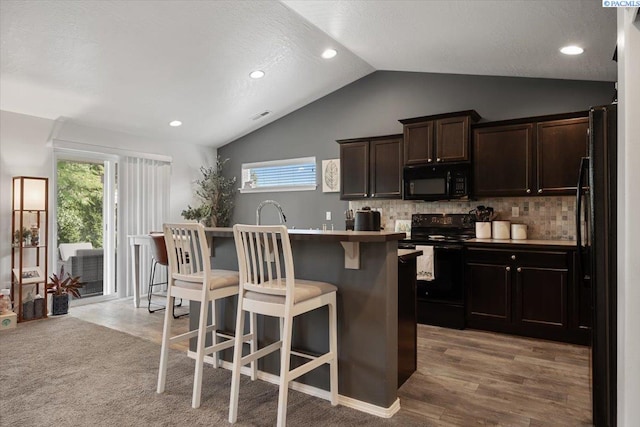 2909 S Jean St, Kennewick, WA 99336 - kitchen with black appliances, a kitchen breakfast bar, vaulted ceiling, dark brown cabinets, and tasteful backsplash