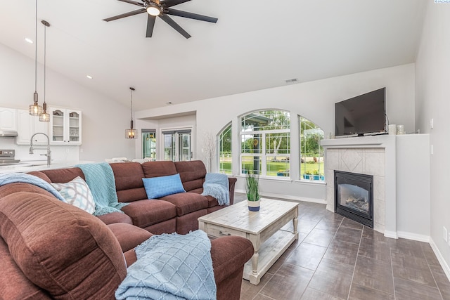 living area with ceiling fan, baseboards, lofted ceiling, a tile fireplace, and visible vents
