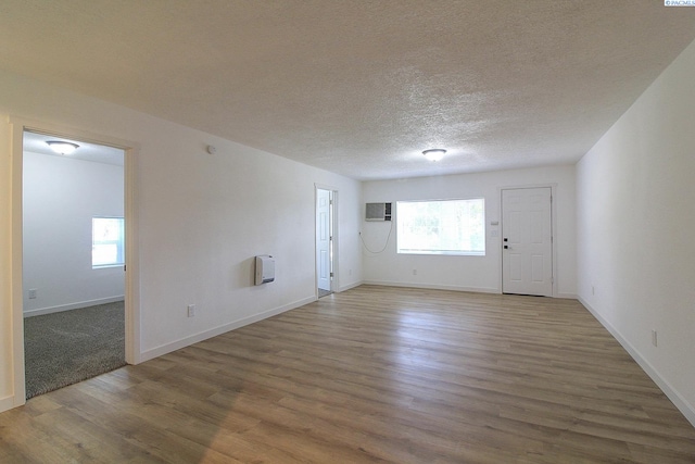 interior space featuring a textured ceiling, an AC wall unit, wood finished floors, and baseboards