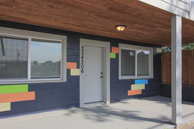 doorway to property with concrete block siding and fence