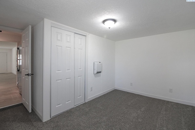 unfurnished bedroom featuring a textured ceiling, a closet, dark carpet, and baseboards