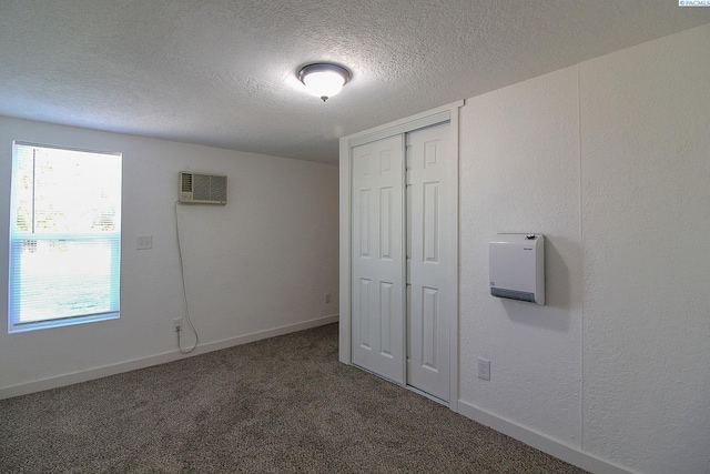 unfurnished bedroom featuring a wall unit AC, a textured ceiling, baseboards, and carpet flooring