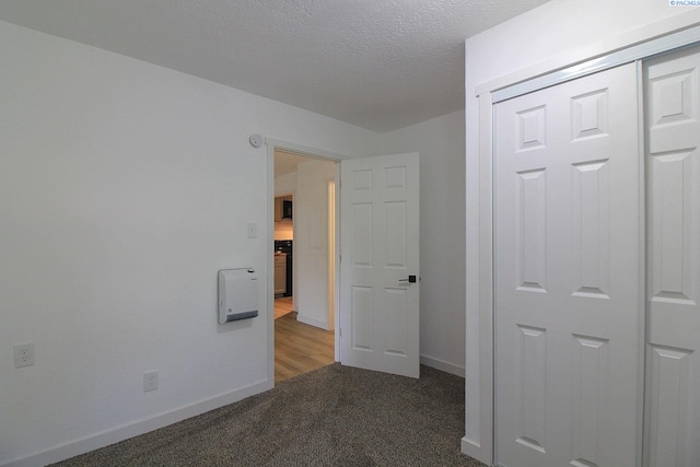 unfurnished bedroom featuring carpet floors, a closet, a textured ceiling, and baseboards