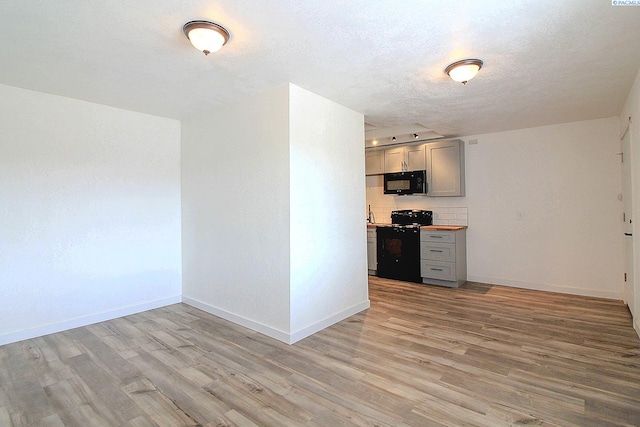 kitchen with black appliances, a textured ceiling, baseboards, and light wood-style floors